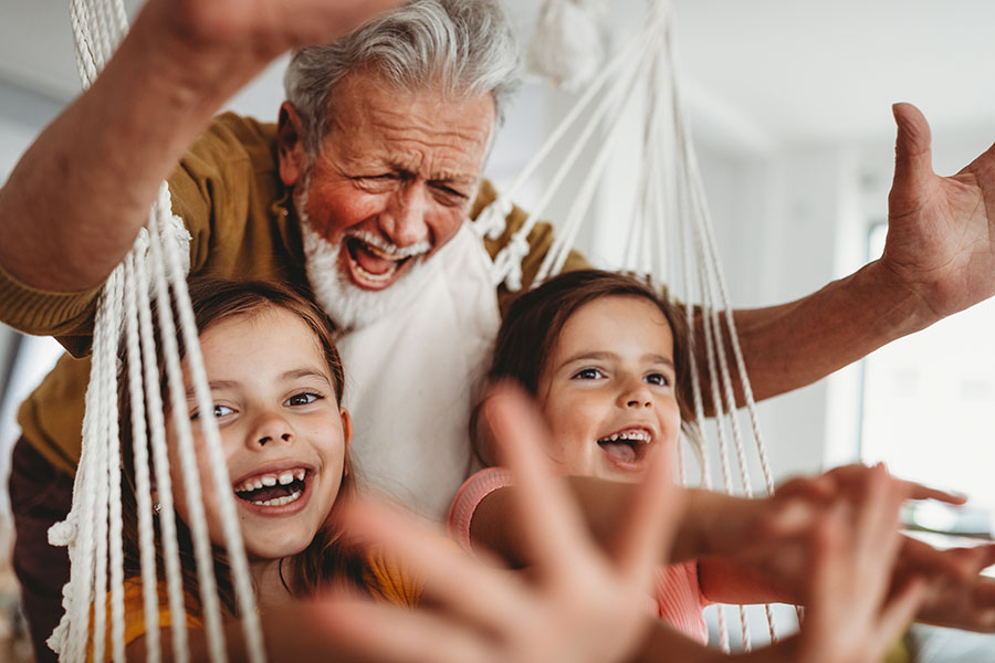 Insurance Quote - Portrait of a Joyful Grandfather Having Fun Swinging His Granddaughters on a Hammock at Home
